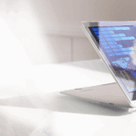 A laptop with a touchscreen displays colorful graphs and data visualizations on a white table in a bright environment.