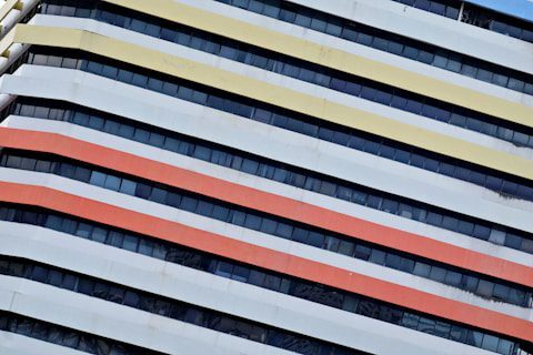 Diagonal stripes in yellow, orange, and red on a white building facade with dark windows.
