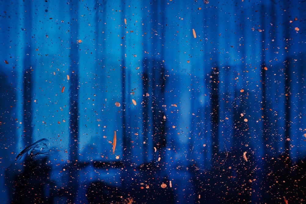 Raindrops and orange particles scattered against a blurred blue background, suggesting a rainy or misty atmosphere.
