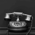 Vintage black rotary telephone with a coiled cord, set against a plain dark background.