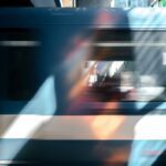 A blurred train moves past with reflections of colorful light; a figure is visible inside one of the windows.