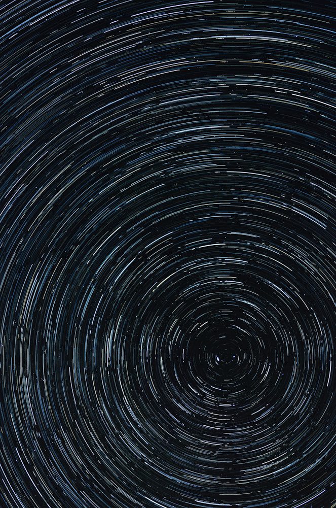 Swirling star trails in a dark night sky, creating circular patterns with varying shades of blue and white.