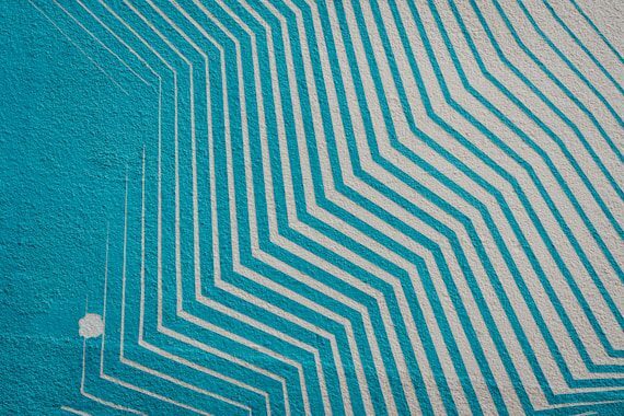Geometric mural with diagonal white lines on a turquoise background, creating a layered, textured pattern.
