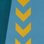 Yellow chevron arrows pointing left on a blue wall, with a textured green panel in the upper portion.