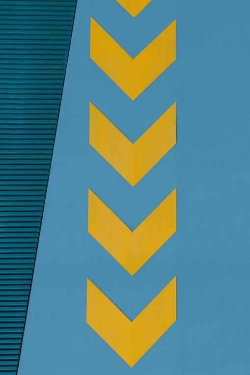 Yellow chevron arrows pointing left on a blue wall, with a textured green panel in the upper portion.