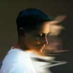 Profile view of a person with short dark hair, wearing a white shirt, with a blurred effect creating a sense of motion.