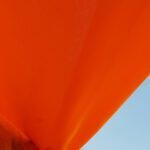 Bright orange fabric drapes diagonally across the image, contrasting with a clear blue sky in the background.