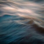 Waves in shades of blue and soft white create a fluid, abstract pattern on the surface of the water.