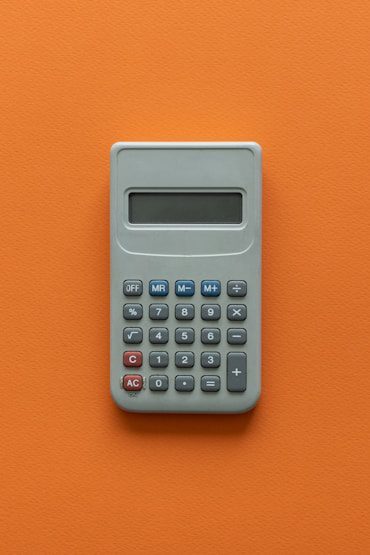 Gray calculator with a digital display, featuring numerical buttons and basic function keys, on an orange background.