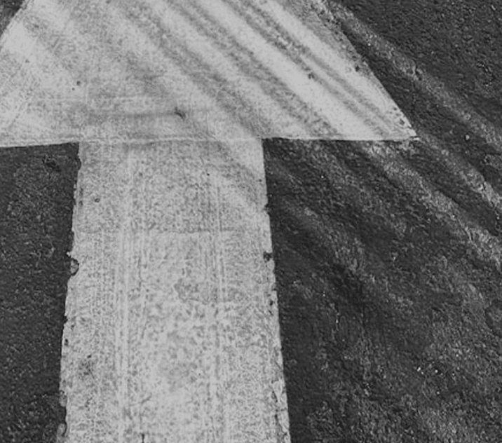 White arrow on a dark asphalt surface, showing signs of wear and tire marks around it.