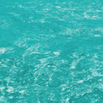 Vibrant turquoise ocean water with gentle ripples reflecting sunlight, creating a shimmering effect.