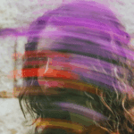 A blurred portrait of a person with long, wavy hair, featuring vibrant streaks of purple, red, and green across the image.