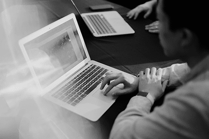 A person with short dark hair is using a laptop, focusing on the screen. Another laptop is visible on the table.