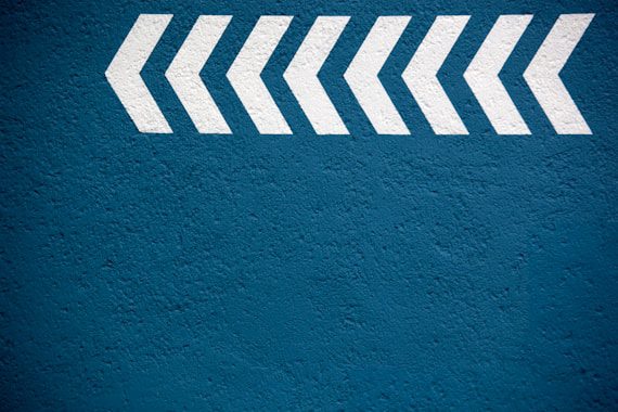 White chevron arrows pointing to the right on a textured blue wall.