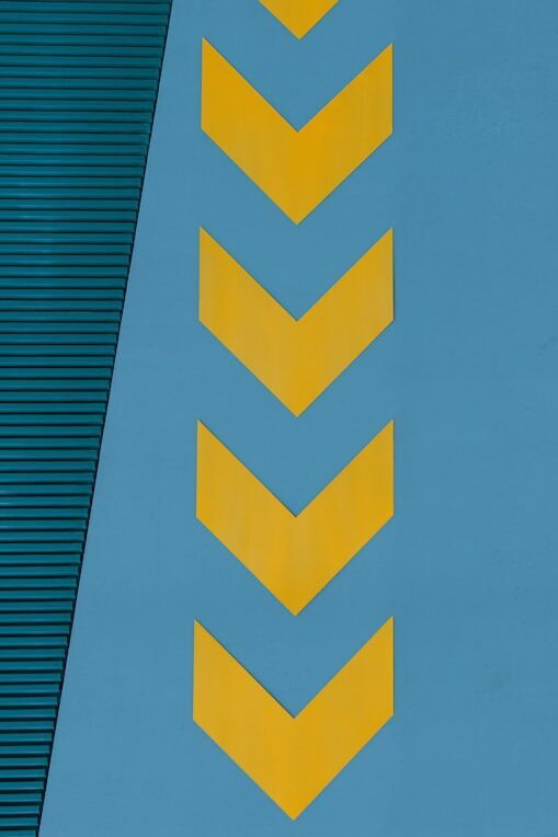 Yellow chevron arrows pointing left on a blue wall, with a textured green panel in the upper portion.