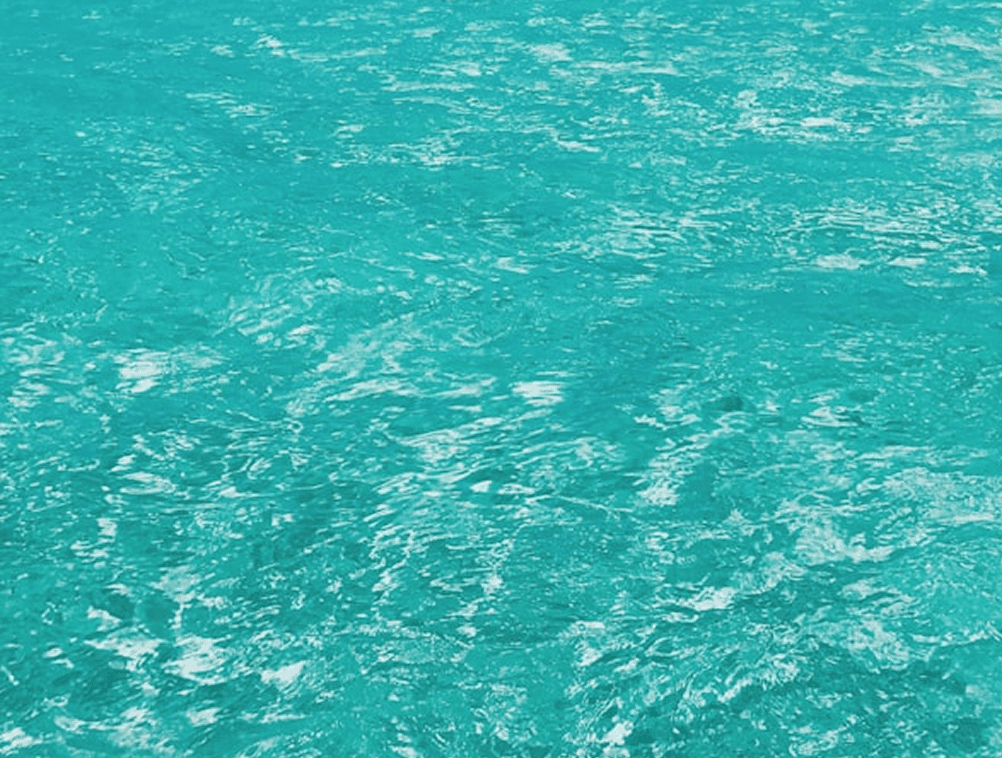 Vibrant turquoise ocean water with gentle ripples reflecting sunlight, creating a shimmering effect.