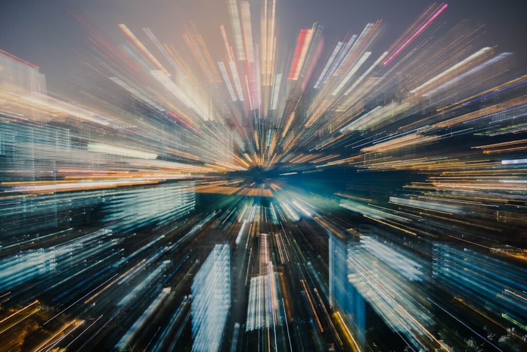 City skyline at night with a zoom effect, showcasing bright lights and blurred buildings in various colors.