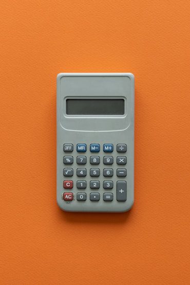 Gray calculator with a digital display, featuring numerical buttons and basic function keys, on an orange background.